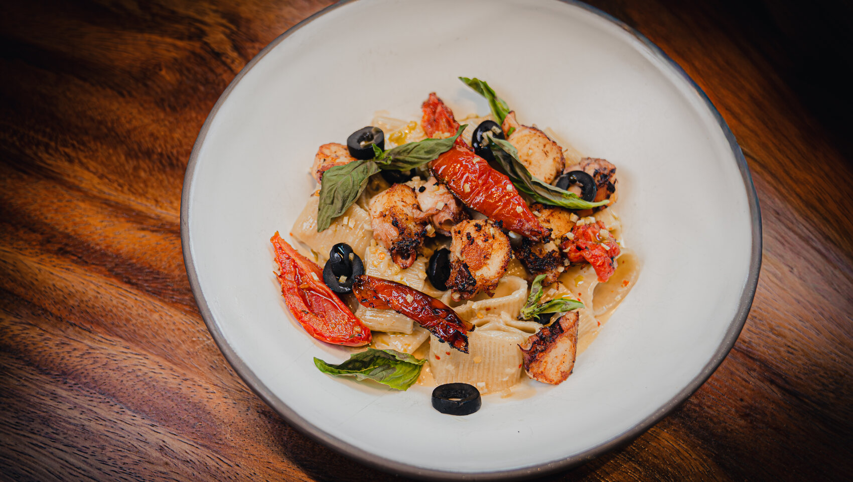 Creamy pasta with grilled seafood, roasted tomatoes, olives, and basil.