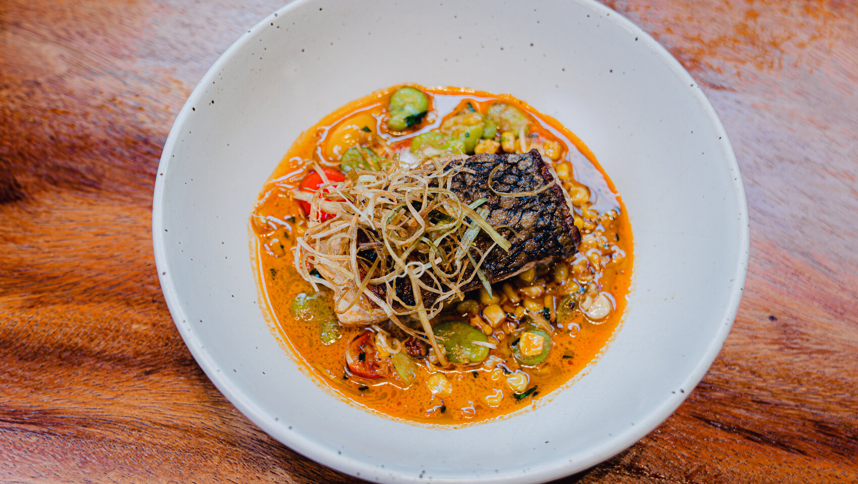 Crispy fish with seasonal vegetables in a vibrant orange broth.